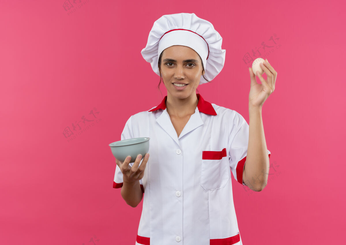 戴着微笑的年轻女厨师穿着厨师制服拿着鸡蛋和碗与复制空间厨师制服厨师