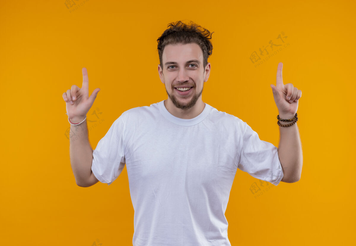 年轻微笑的年轻人穿着白色t恤指向孤立的橙色背景上小伙子T恤橙色