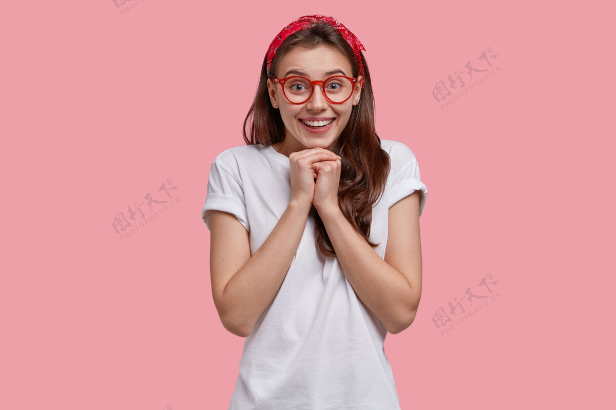 牙关快乐少女的上身镜头 笑容灿烂 双手合十 下巴下 戴着红色头带和休闲t恤欢呼眼镜高兴