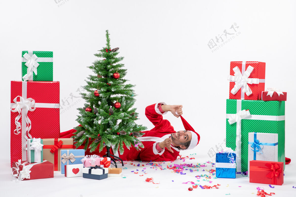 圣诞老人节日气氛与年轻的圣诞老人躺在圣诞树后靠近礼物的白色背景股票照片圣诞老人股票礼物