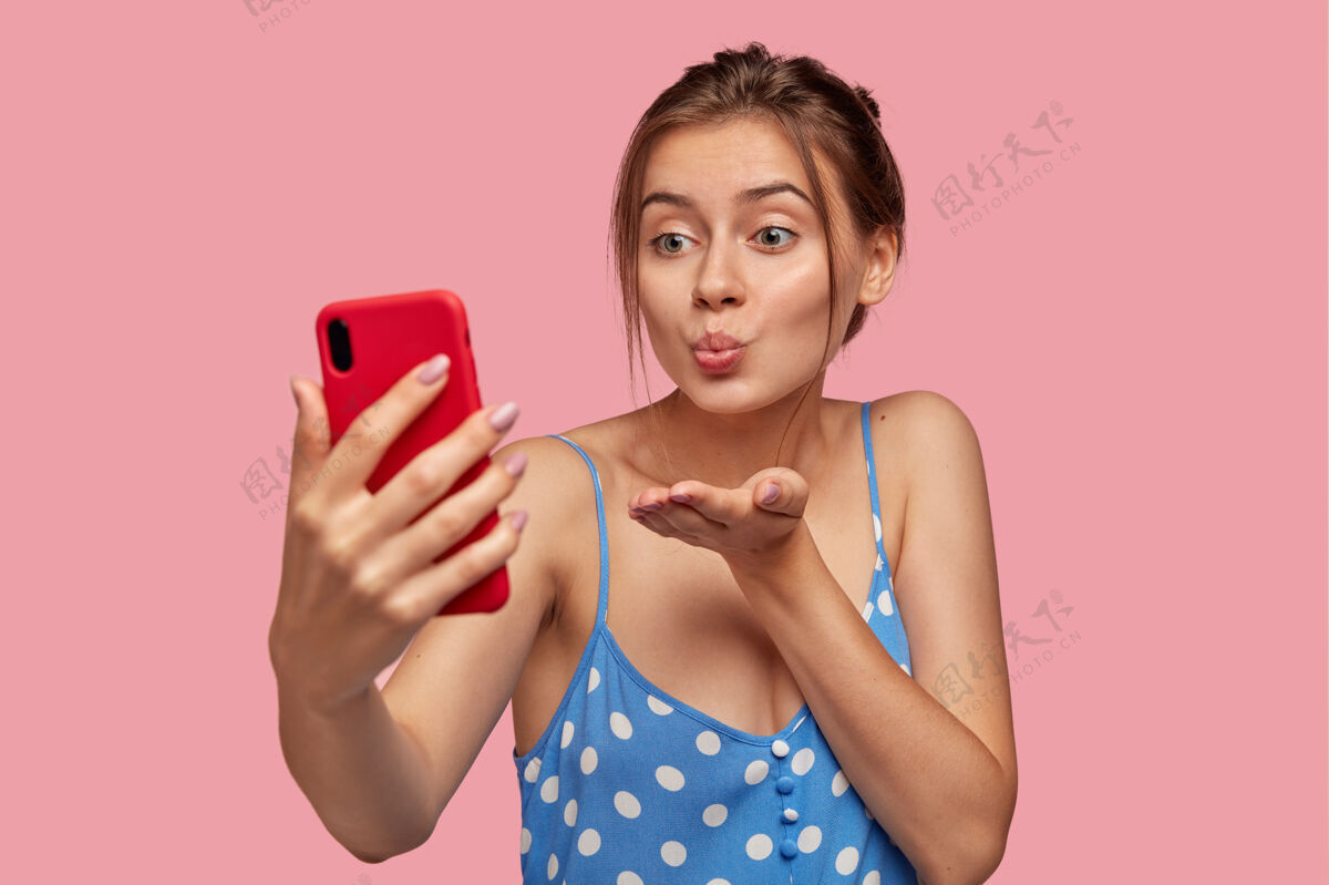 接吻帅气的女朋友通过智能手机和男人调情 视频通话时空中接吻 手持手机 穿着休闲夏装坐着视频通话智能手机