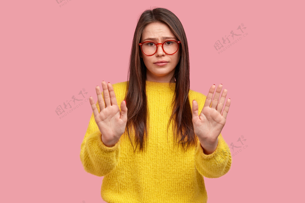 摆姿势美女照片向镜头举手 做警告标志或限制手势 戴眼镜和黄色套装防御不高兴警告