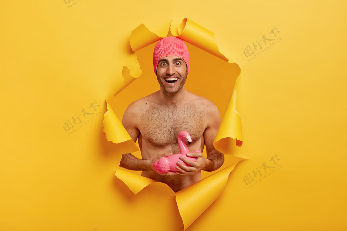 娱乐暑假的概念快乐的男人 良好的体形 赤裸的躯干站立 穿着粉色泳衣 手持充气火烈鸟携带停留家伙