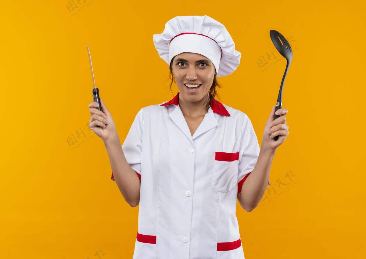 女面带微笑的年轻女厨师身穿厨师制服 手持抹刀和刀 留有复印空间戴着制服刀