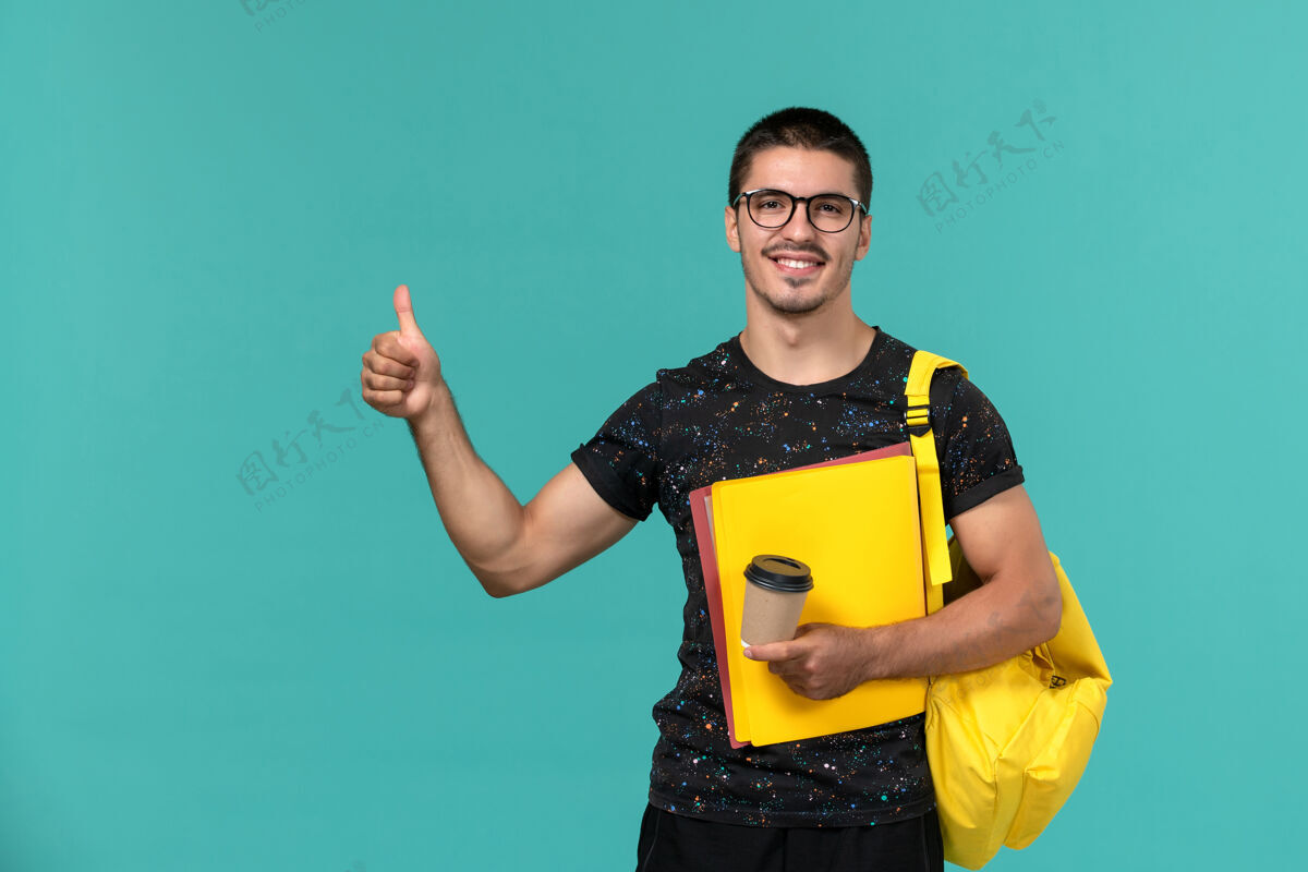 文件前视图中的男学生穿着深色t恤黄色背包 蓝色墙上放着不同的文件和咖啡教训大学不同