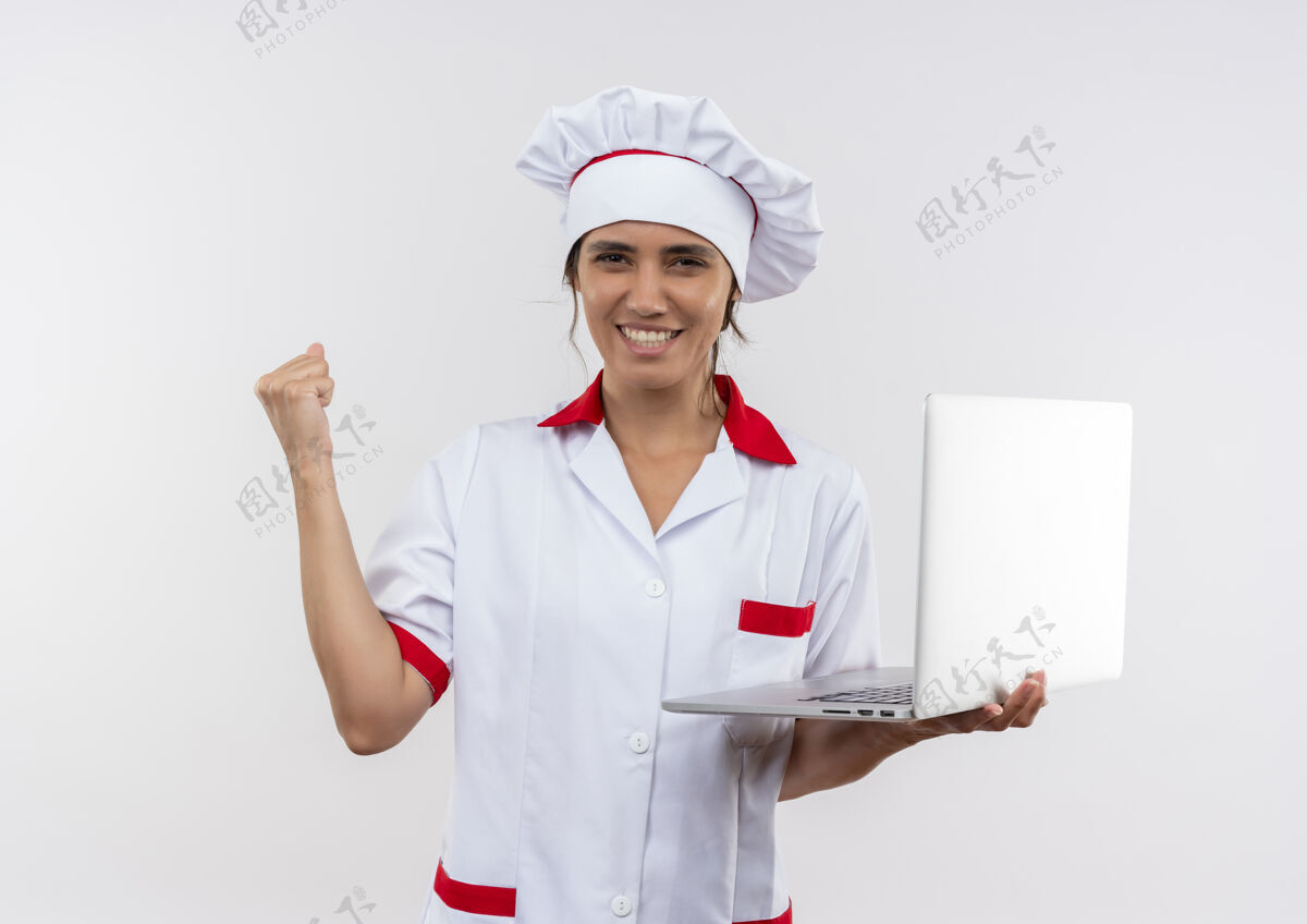 手势快乐的年轻女厨师穿着厨师制服 手持笔记本电脑 在隔离的白色墙壁上显示“是”的手势 并留有复印空间穿着拿着厨师
