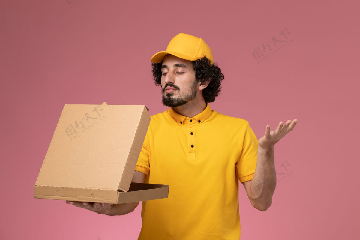 服务正面图：身穿黄色制服的男快递员拿着食品快递箱站在浅粉色的墙上人送货视图