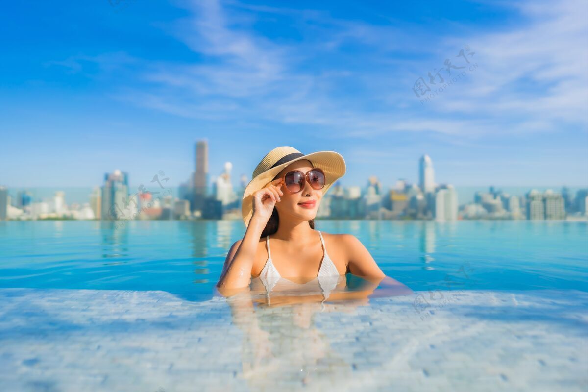 高肖像美丽的亚洲年轻女子微笑放松休闲围绕室外游泳池与城市景观顶部屋顶著名