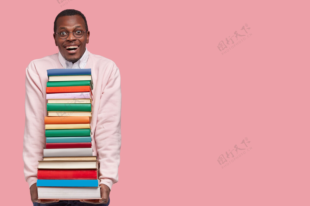 堆穿着休闲套头衫的迷人微笑的快乐黑人男子拿着从图书馆借来的一堆书的照片堆持有非洲