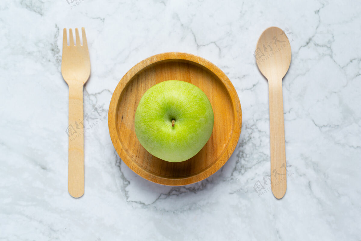 绿色把青苹果放在木碗里 旁边放一个木勺和叉子有机食品青苹果