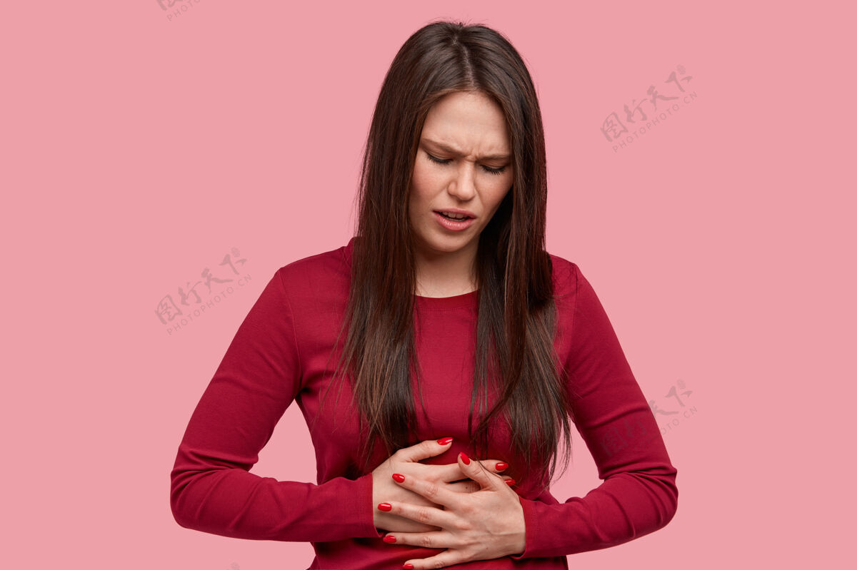 不好沮丧的黑发女人 表情不悦 手放在肚子上 感觉像有月经一样痛 穿着红色毛衣疼痛发炎烦恼