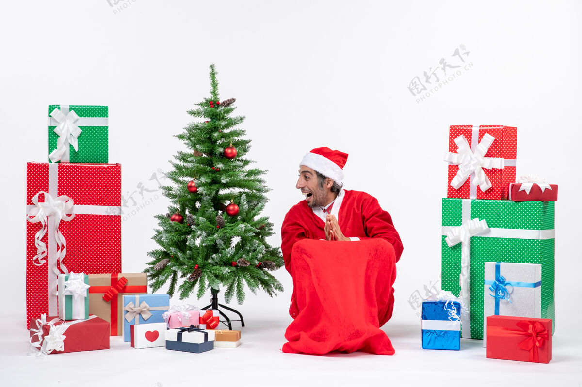 礼物情绪激动的年轻人打扮成圣诞老人与礼物和装饰圣诞树上的白色背景镜头圣诞圣诞老人男人