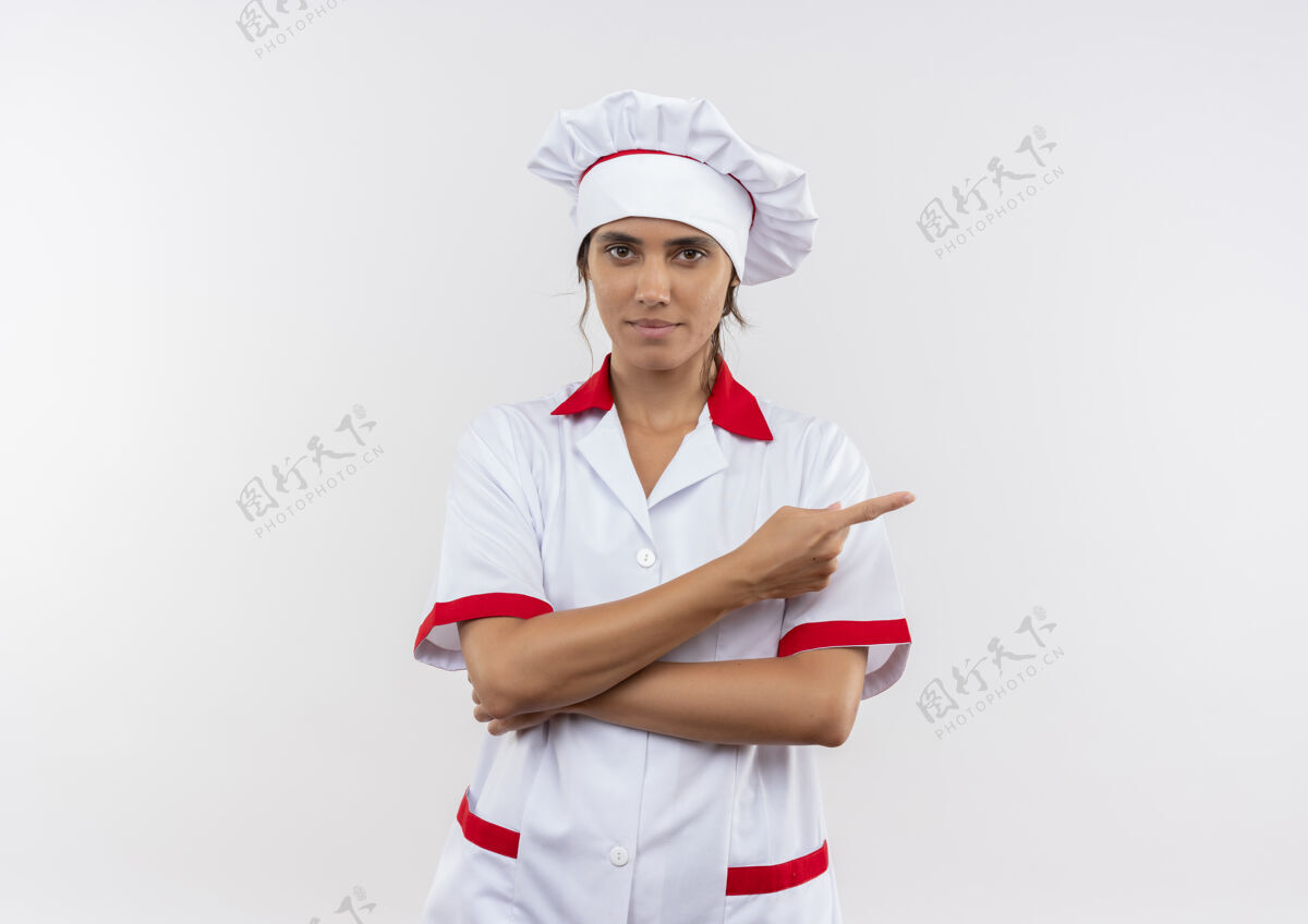 分年轻的女厨师穿着厨师长的制服 高兴地指着旁边的白色隔离墙与复印空间厨师高兴制服