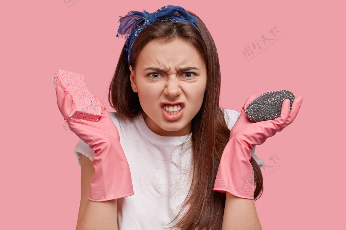 清洁不高兴的黑发家庭主妇对家里的许多工作很生气 戴着粉红色的橡胶手套 不喜欢咬紧牙关橡胶T恤头带