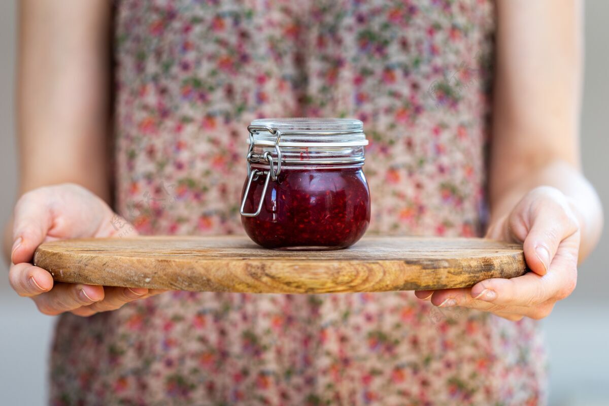 自制一个女人拿着一个自制的纯素生树莓果酱 放在一个玻璃罐里 放在木制的表面上粉色表面木制