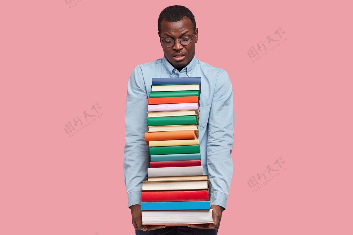 不满不高兴的非裔美国科学家或学生背着厚厚的一堆教科书 穿着优雅的衬衫墙壁男性眼镜