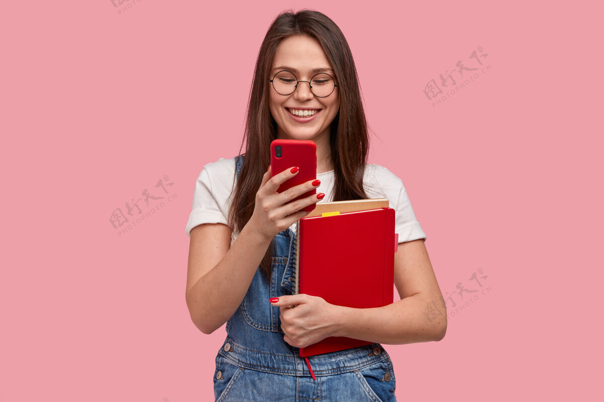 高兴漂亮的黑发女人拿着手机 发短信 开心的看帖子下的评论 拿着课本工作服笔记本乐观