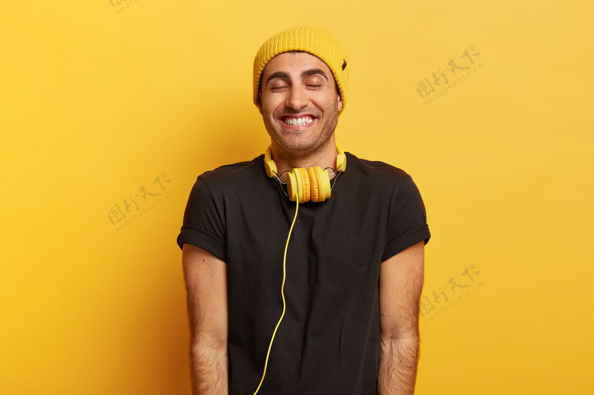 音乐脖子上戴着耳机的帅哥 笑得很开心 闭上眼睛 戴着帽子和黑色t恤情感满足满意