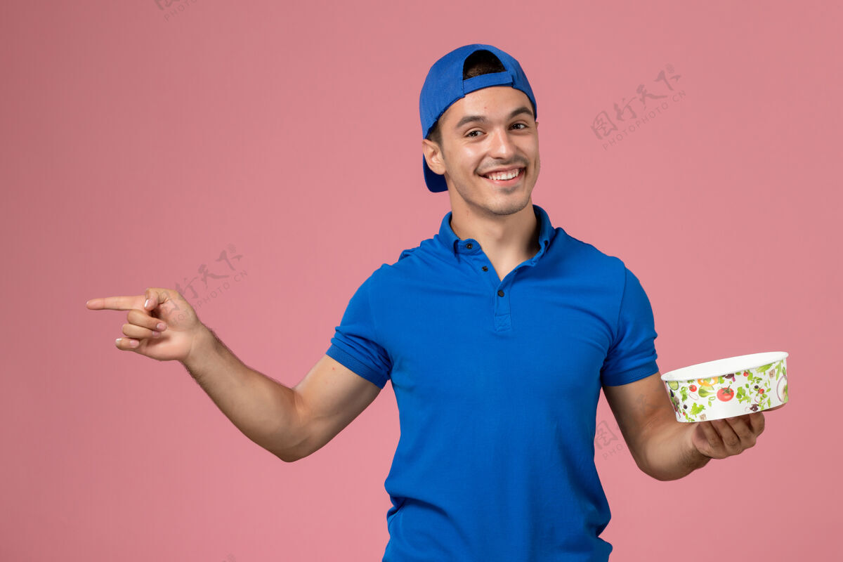 男性正面图身穿蓝色制服披肩的年轻男性信使手持浅粉色墙上的圆形投递碗圆人递送