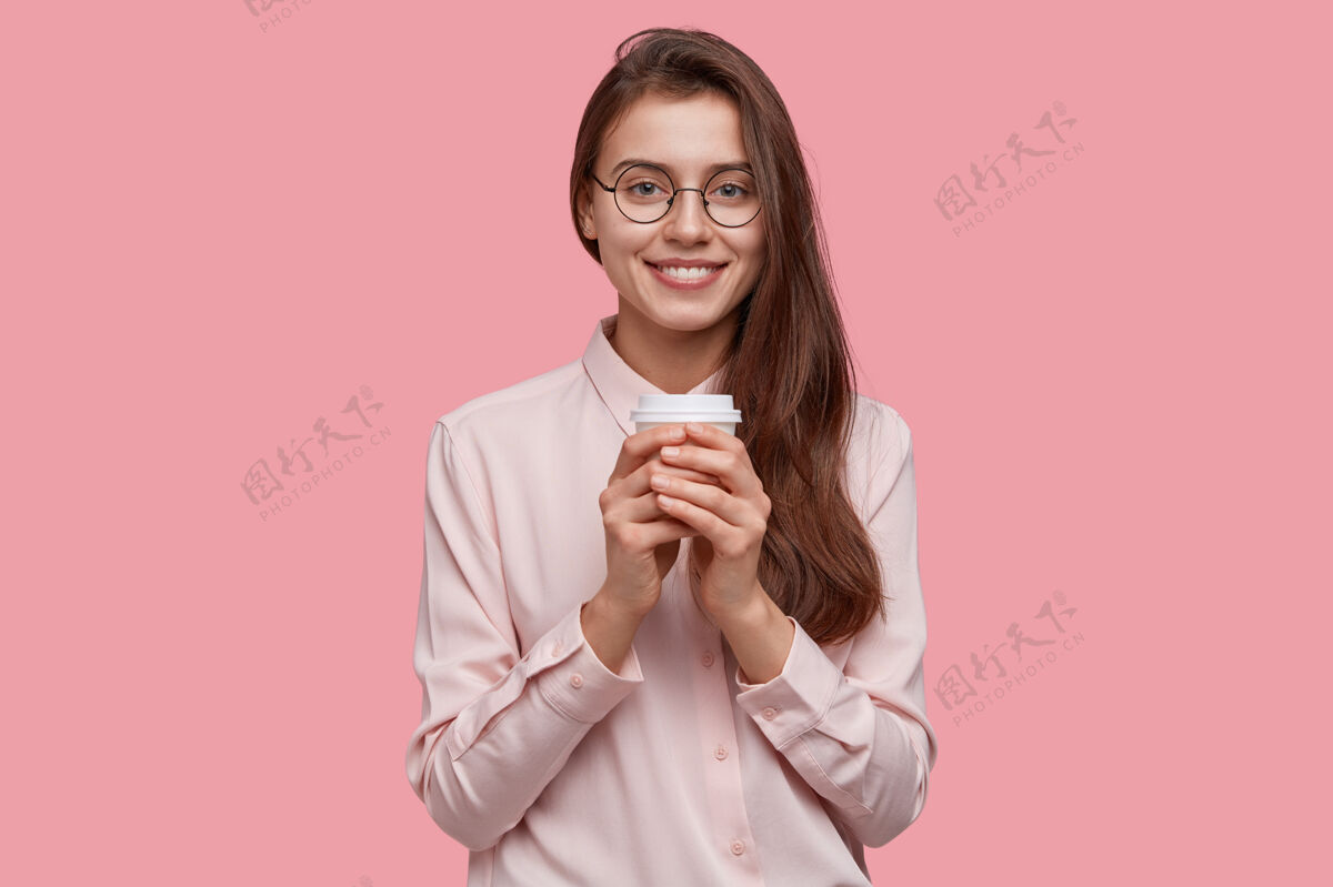 高兴正面女学生摄影棚卓有成效地抓起咖啡工作 端着饮料纸杯 逛咖啡馆 穿正式衬衫温暖学生高兴