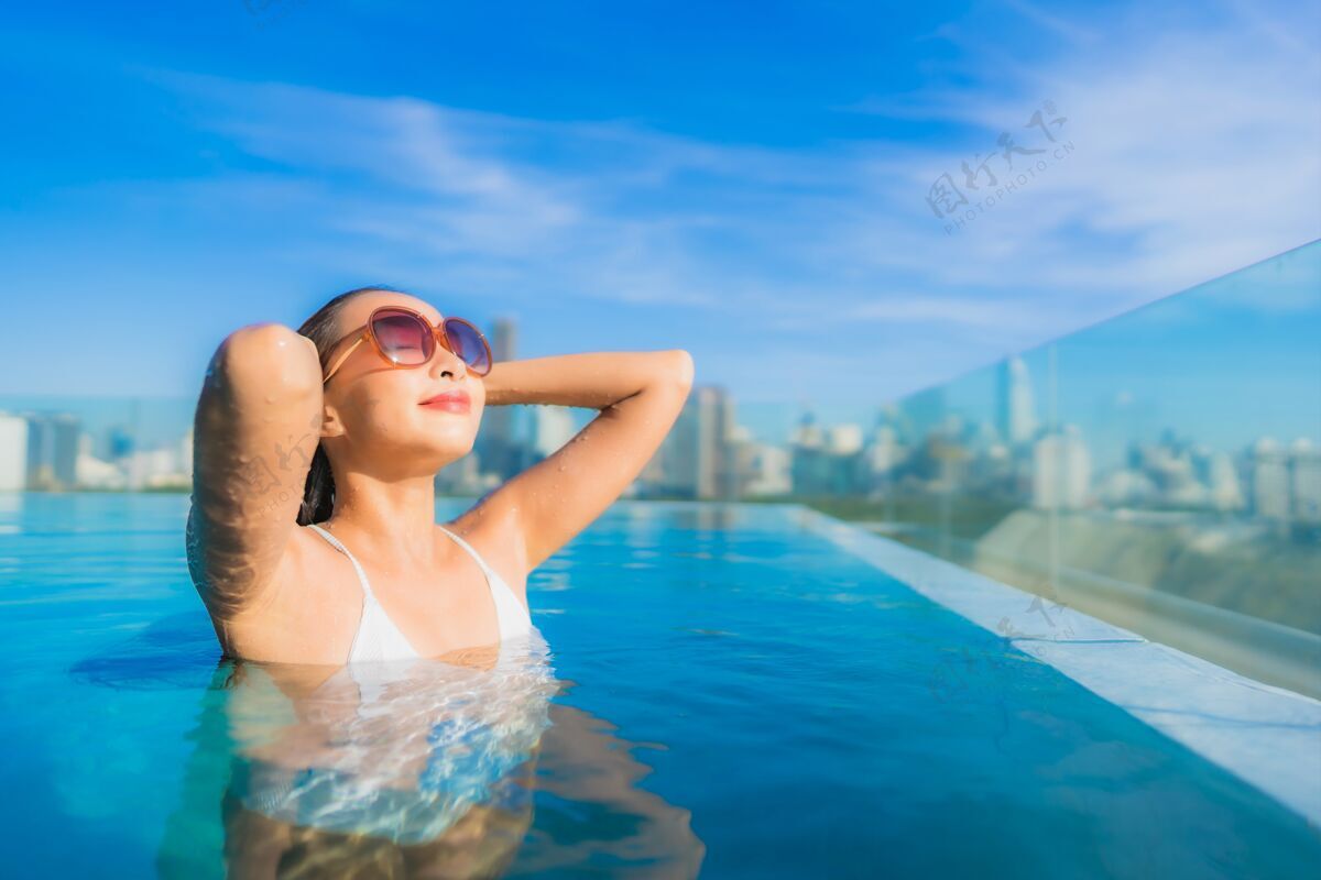 屋顶肖像美丽的亚洲年轻女子微笑放松休闲围绕室外游泳池与城市景观度假村城市屋顶