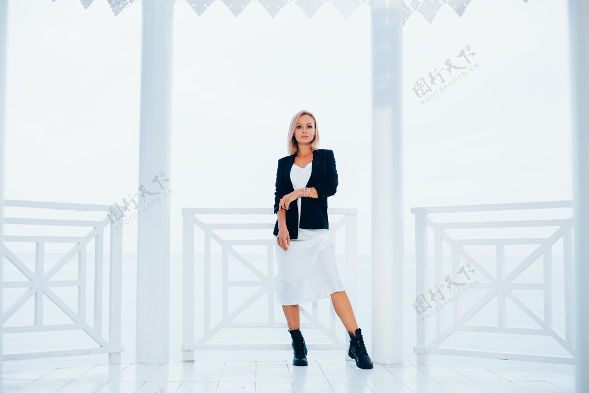 肖像时尚写真时尚的白种女人在丝绸长裙黑色外套和大靴子在豪华的地方与海景西装黑色长