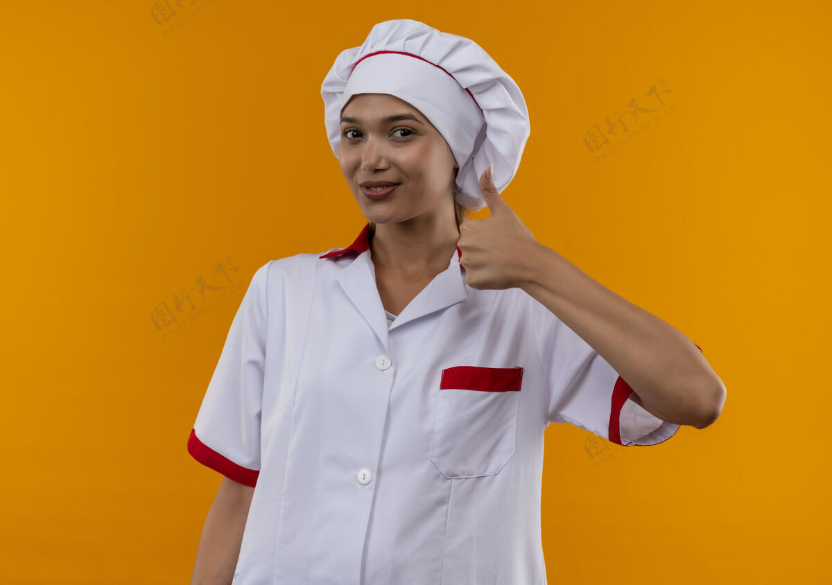 制服高兴的年轻厨师女穿厨师制服 她的大拇指上孤立的橙色墙壁厨师厨师拇指