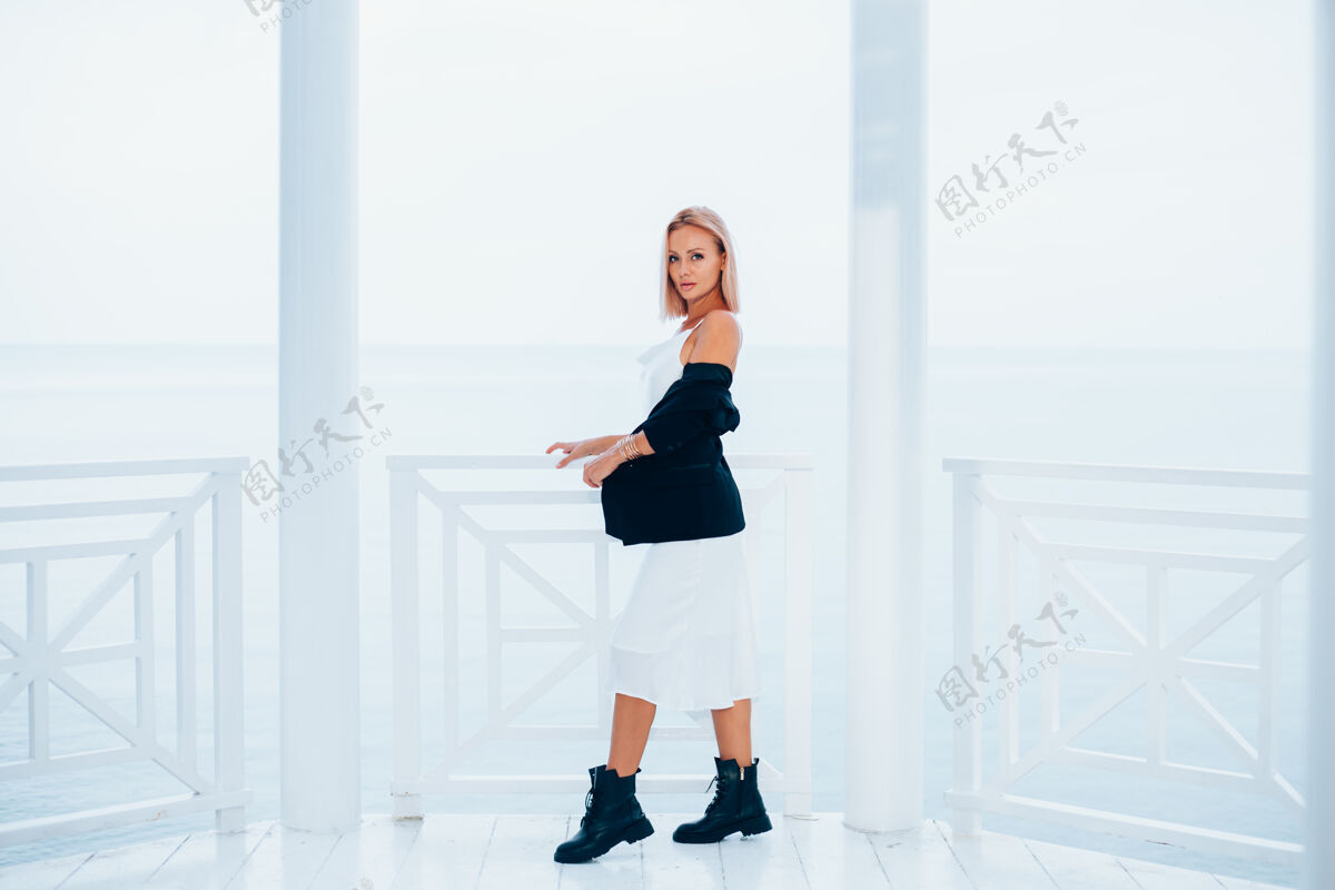 女士时尚写真时尚的白种女人在丝绸长裙黑色外套和大靴子在豪华的地方与海景年轻长度丰满