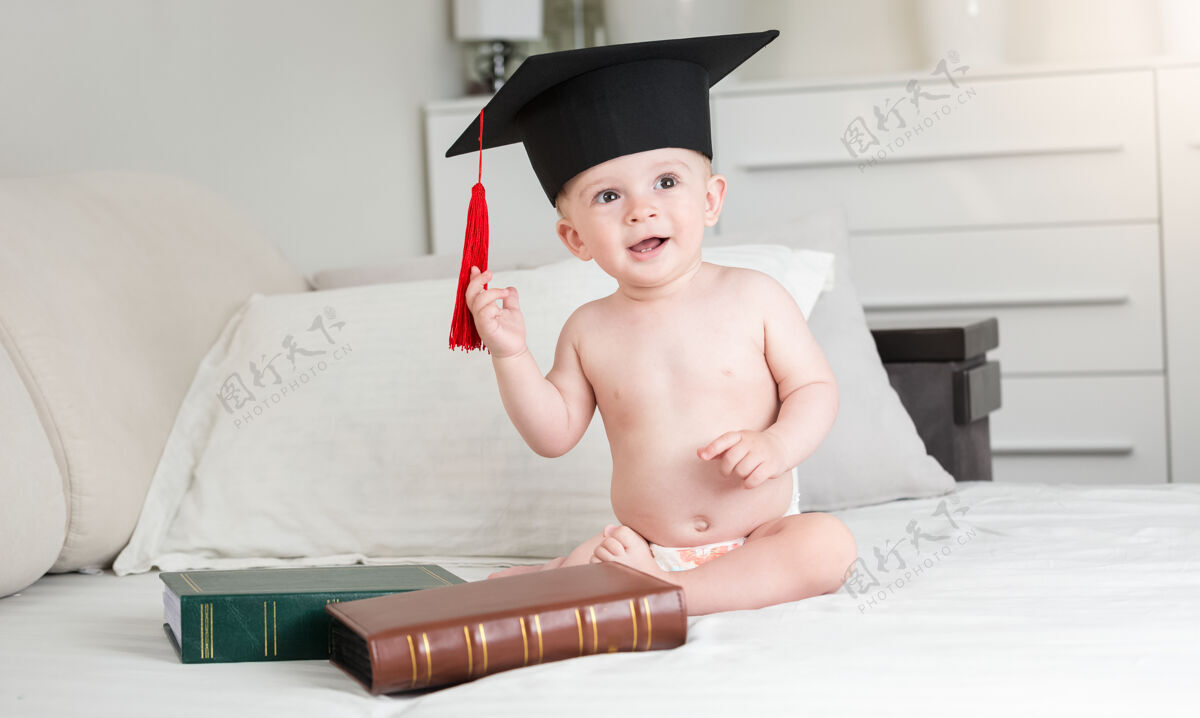 家庭穿着尿布 戴着黑色毕业帽的滑稽男婴的画像年轻知识尿布
